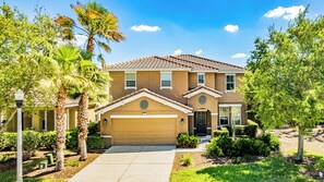 A two-story house with a brown facade, a garage, and a well-maintained lawn with palm trees. - Solterra Luxury Oasis: Resort Fees Included (Davenport)