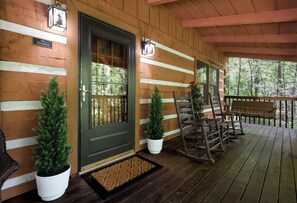 A wooden porch with a bench, chairs, and potted plants.