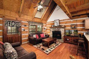 Ein gemütliches Cabin-Interieur mit Holzbalkendecke, Kamin, einer Couch, einem Couchtisch und einem Kamin aus Stein.