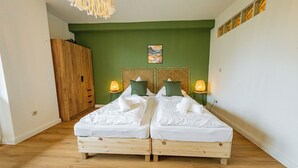 Una habitación con dos camas de madera, paredes verdes, un armario de madera y un cuadro en la pared.