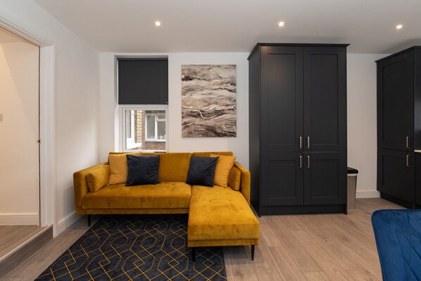 A modern living room with a mustard-colored sofa, a black and yellow patterned rug, and dark wooden cabinets. - Woodside Park 3 Bedroom Apt with Parking (London)