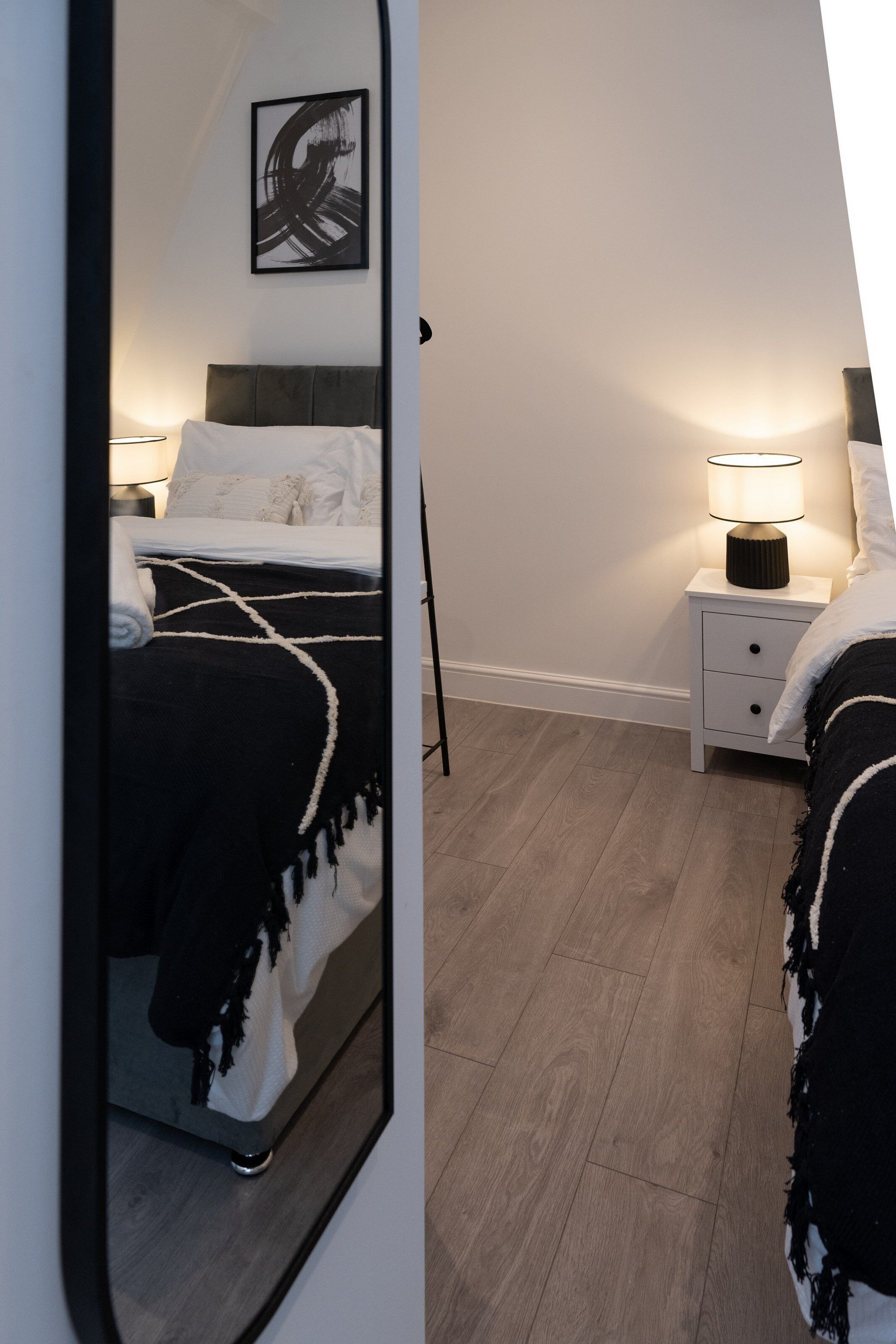 Un dormitorio con cama, mesitas de noche, lámpara y espejo.