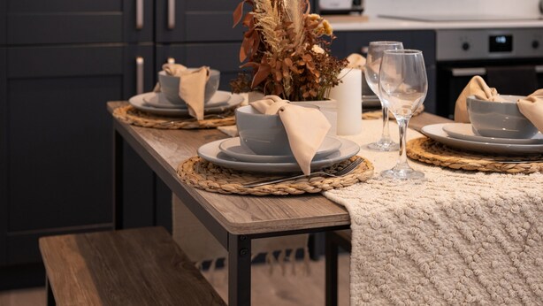 A dining table set with plates, bowls, napkins, and a vase of dried flowers. - Woodside Park 3 Bedroom Apt with Parking (London)