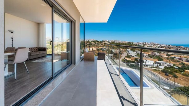 A modern balcony with a glass railing overlooking a cityscape and a pool.