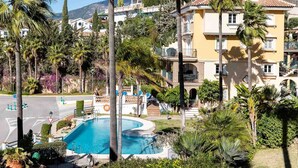 Zona residencial con piscina rodeada de palmeras y un edificio con balcones.
