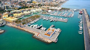Una marina con numerosos barcos amarrados, un edificio grande con techo rojo y un paisaje urbano al fondo.