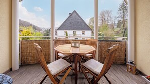 Un espacio al aire libre cubierto con una mesa y sillas de madera, vista a una casa y cerca de bambú.
