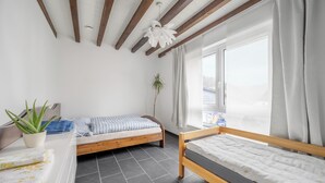 Un dormitorio con dos camas, una planta en maceta, una ventana con cortinas y un ventilador de techo.