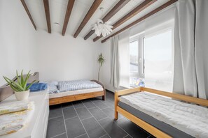 A bedroom with two beds, a potted plant, a window with curtains, and a ceiling fan.