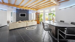Un interior moderno con un sofá, una mesa de comedor, sillas, un televisor y un ventanal grande.