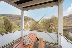 Un balcón con una mesa de madera, un farol y vistas a una zona boscosa.