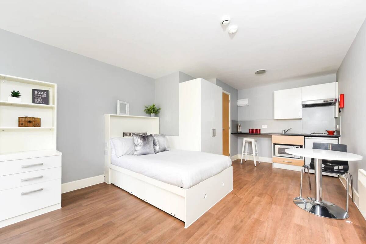 A modern apartment with a bed, kitchenette, and a small dining area.