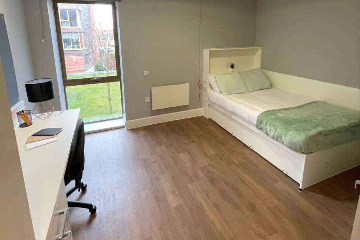 A bedroom with a bed, a desk, and a radiator.