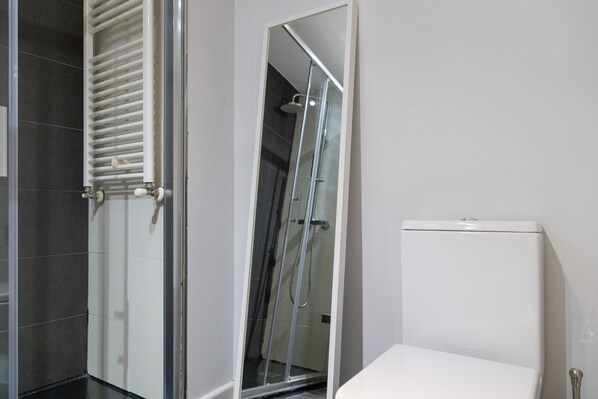 A bathroom with a glass shower enclosure, a white toilet, and a towel rack.