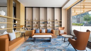 A modern living room with a sofa, armchairs, and a coffee table. There are shelves with decorative items and a view of buildings through large windows. - Fairfield By Marriott Yangshuo (Guilin)