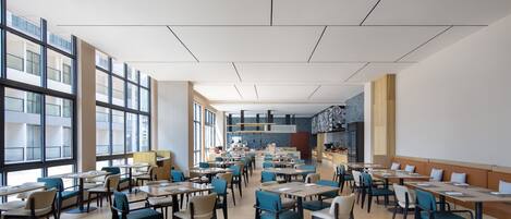 A spacious dining area with multiple tables and chairs, large windows, and a modern ceiling design.