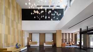 A modern lobby with a marble floor, wooden reception desks, and a hanging light fixture. - Fairfield By Marriott Yangshuo (Guilin)