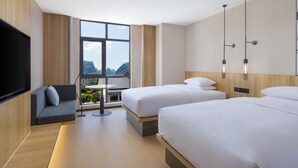 A modern hotel room with two beds, a TV, a sofa, and a large window offering a mountain view. - Fairfield By Marriott Yangshuo (Guilin)