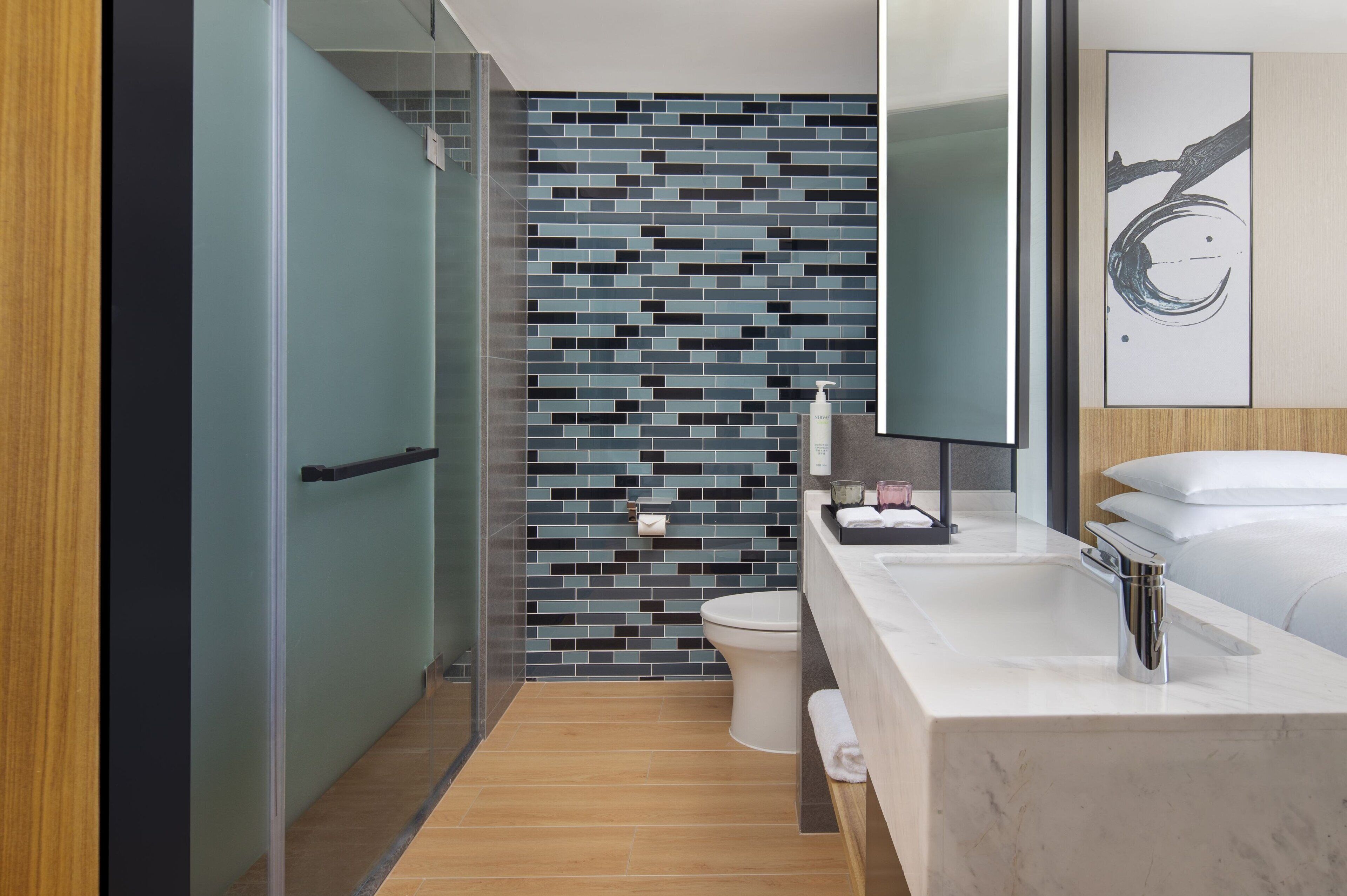 A modern bathroom with a tiled backsplash, a glass shower enclosure, a white toilet, and a marble sink with a mirror above it.