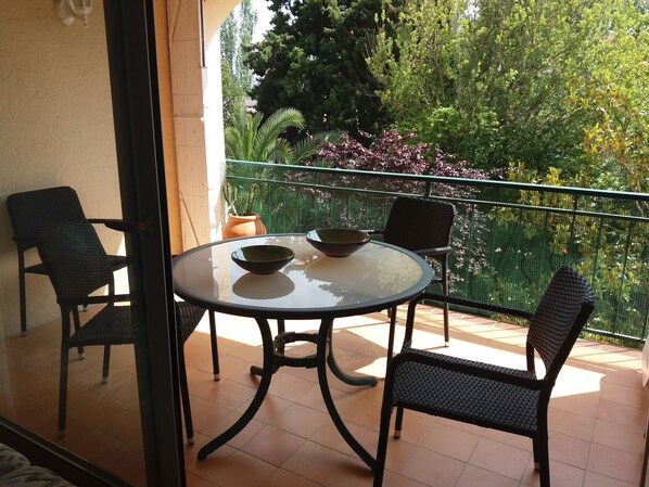 Ein Balkon mit rundem Glastisch, zwei Stühlen und einem Blumentopf.