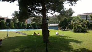 A well-maintained grassy area with a swimming pool, a large tree, and a lamp post. - FULLY EQUIPPED APARTMENT IN ONE OF THE BEST BEACHES ON THE COSTA BRAVA (Sant Feliu de Guíxols)