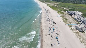 Oversigtsbillede af en strand med mennesker, parasoller og parkerede biler.