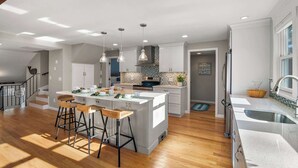 A modern kitchen with a central island, bar stools, and pendant lighting. - Updated A-Frame w/ Game Room, Short Drive to Beach! (Barnstable)