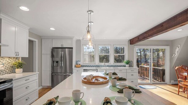 A modern kitchen with white cabinetry, a stainless steel refrigerator, and a central island with a breakfast setup. - Updated A-Frame w/ Game Room, Short Drive to Beach! (Barnstable)