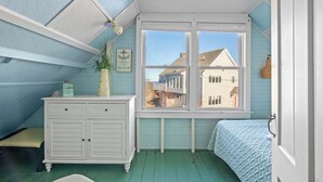 A bedroom with a window, a dresser, a bed, and a view of houses outside. - Walk to Private Bayside Beach! (Brewster)