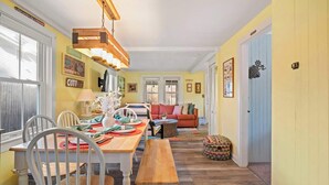 A dining area with a wooden table, chairs, and a bench. There is a sofa and a patterned ottoman in the background. - Walk to Private Bayside Beach! (Brewster)