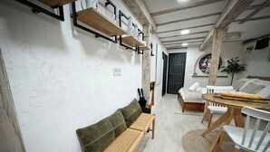 A cozy room with a wooden bench, a bed with white bedding, a dining table with chairs, and a wall-mounted shelf with decorative items. - St. John of the Cross Studio (San Sebastián de Garabandal)
