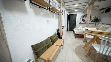 Une pièce chaleureuse avec un banc en bois, un lit recouvert de linge de maison blanc, une table à manger avec des chaises et une étagère murale agrémentée d’objets décoratifs.