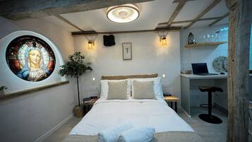 Une chambre à coucher avec un lit, un bureau et une chaise. Il y a une fenêtre ornée de vitraux et une plante.
