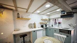 A kitchen with white tiled walls, wooden beams, a round dining table, and a built-in oven. - St. John of the Cross Studio (San Sebastián de Garabandal)