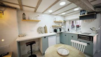 Une cuisine aux murs recouverts de carreaux blancs, avec des poutres en bois, une table à manger ronde et un four encastré.