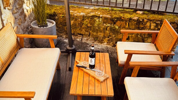 A wooden deck with a table, two cushioned chairs, and a potted plant. - St. John of the Cross Studio (San Sebastián de Garabandal)