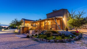 Una casa a due piani con una scala in legno che conduce all'ingresso, circondata da un vialetto sterrato e un giardino curato.