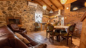 Un accogliente soggiorno con parete in pietra, divano in pelle, tavolo da pranzo con sedie e camino.