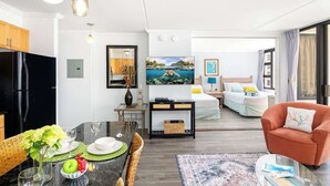 A modern hotel room with a dining area, a bed with a view, and a living area with a sofa and armchair. - Ocean-view condo steps from Waikiki Beach (Honolulu)