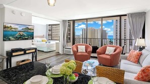 A modern living room with a large window, a flat-screen TV, a dining area, and a sofa. - Ocean-view condo steps from Waikiki Beach (Honolulu)