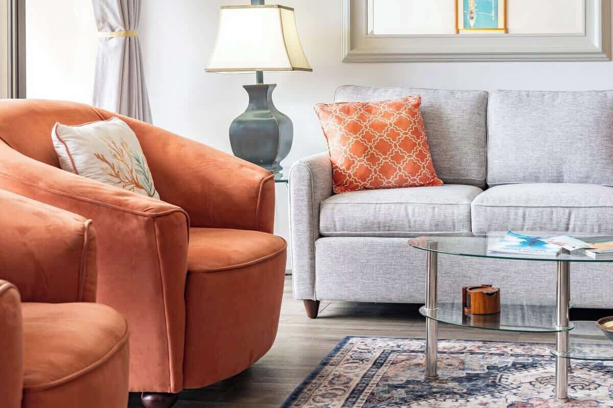 Un salon comprenant un canapé, un fauteuil, une table basse en verre et une lampe.