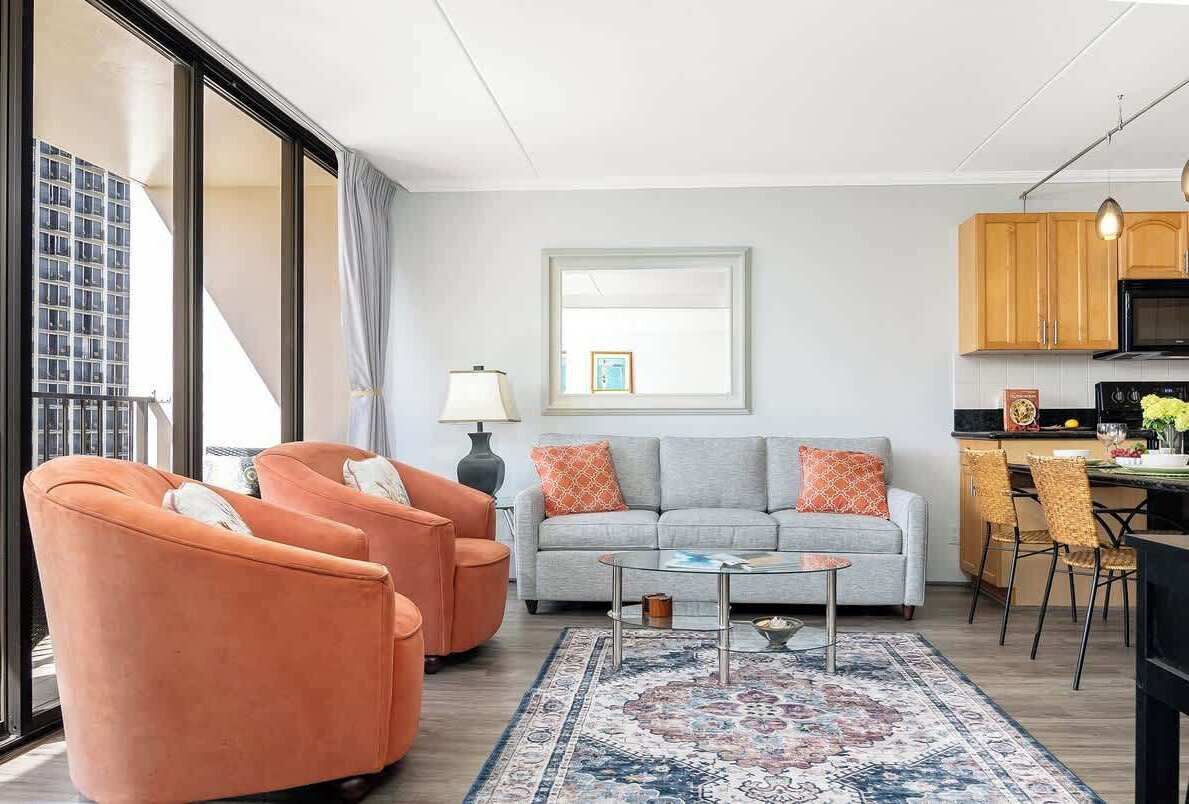 A modern living room with a sofa, armchairs, a coffee table, and a kitchen area with cabinets and a microwave.