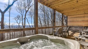 A wooden deck with a hot tub, outdoor seating, and a view of a snowy forest. - Pet Friendly, Ellijay cabin rental with a big view of the Georgia Mountains! Hot tub, outdoor fireplace (Ellijay)