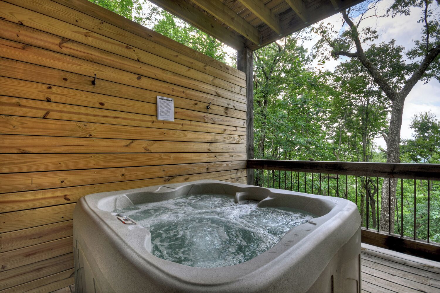 A hot tub on a wooden deck with a wooden railing and trees in the background.