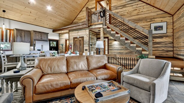 A spacious living room with a wooden ceiling, a leather sofa, a grey armchair, and a coffee table with magazines. - Pet Friendly, Ellijay cabin rental with a big view of the Georgia Mountains! Hot tub, outdoor fireplace (Ellijay)