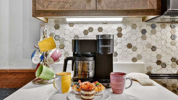 A kitchen with a coffee maker, colorful mugs, and a hexagonal tile backsplash. - Pet Friendly, Ellijay cabin rental with a big view of the Georgia Mountains! Hot tub, outdoor fireplace (Ellijay)