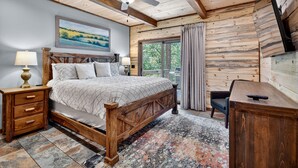 A bedroom with a wooden bed, a desk, a ceiling fan, and a large window with curtains. - Pet Friendly, Ellijay cabin rental with a big view of the Georgia Mountains! Hot tub, outdoor fireplace (Ellijay)