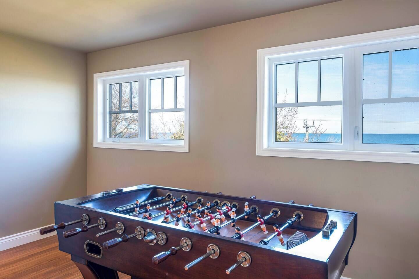 Une pièce avec une table de baby-foot, deux fenêtres et un plancher en bois.