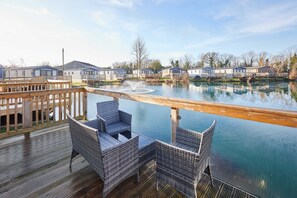 Una terraza con mobiliario de mimbre con vista a un cuerpo de agua tranquilo, con casas móviles al fondo.