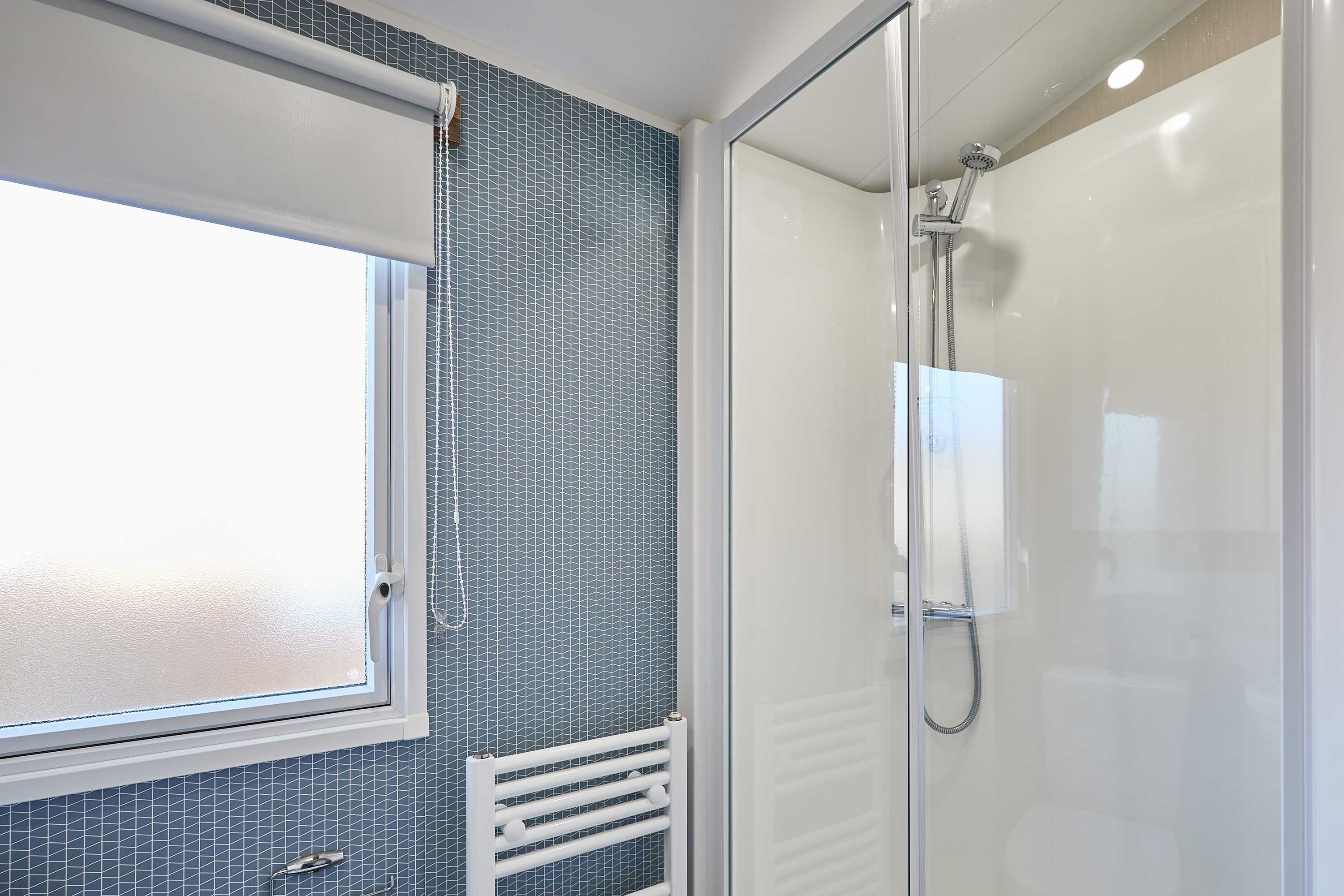 A bathroom with a shower, a window, and a tiled wall.